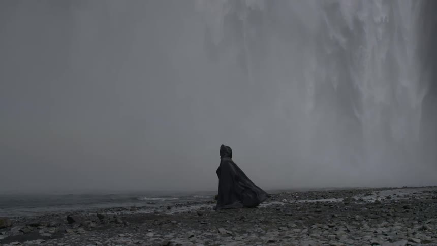 A cloaked figure stands near a waterfall