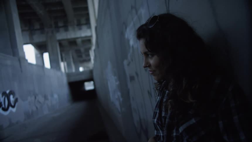 Woman leans against concrete graffiti covered wall under bridge