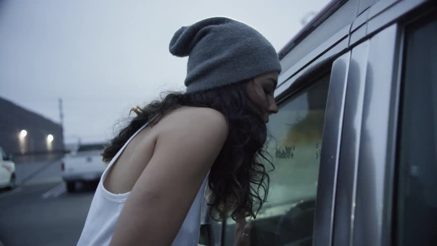 Woman stands and looks inside the car at dusk