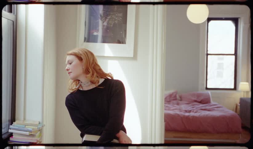 A young woman holding a book leans over and looks out the window