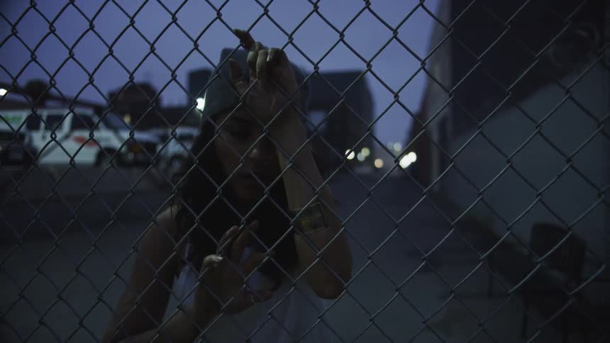 Woman leans on wired fence on the streets at night