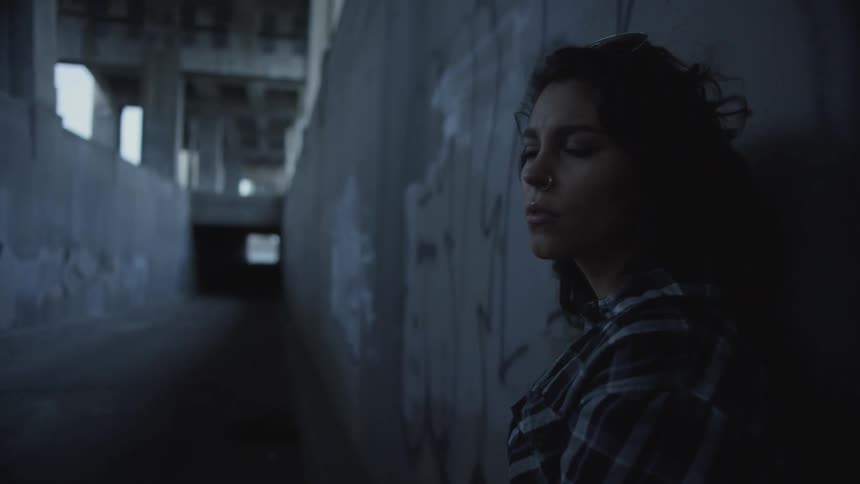 Woman leans against the wall of an interior tunnel