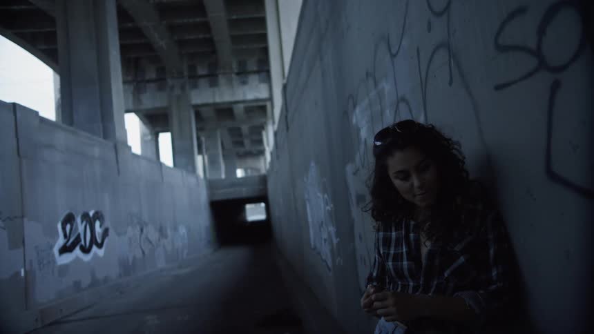 A woman leaning against a graffiti covered wall under a bridge