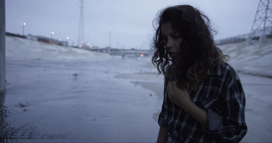A woman stands outside in a remote area of a town looking depressed and nervous