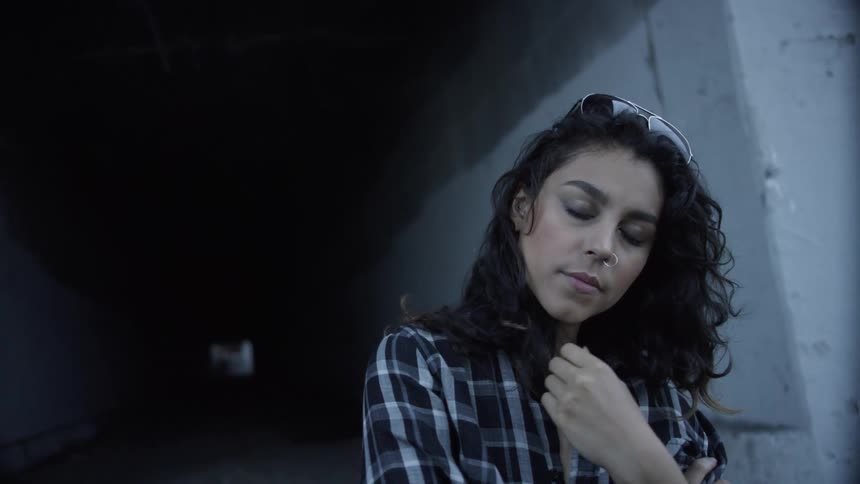 Woman stands in a tunnel with her eyes closed as she plays with her hair