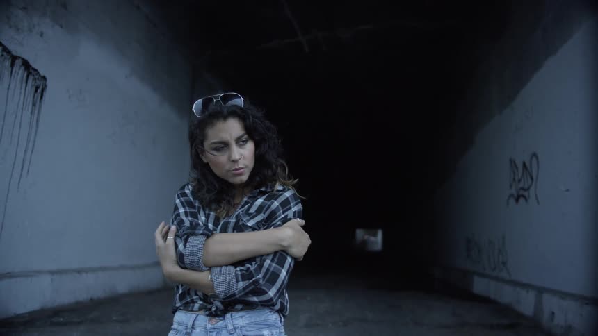 A young woman stands outside and rubs her arms with her hands as if too warm herself up