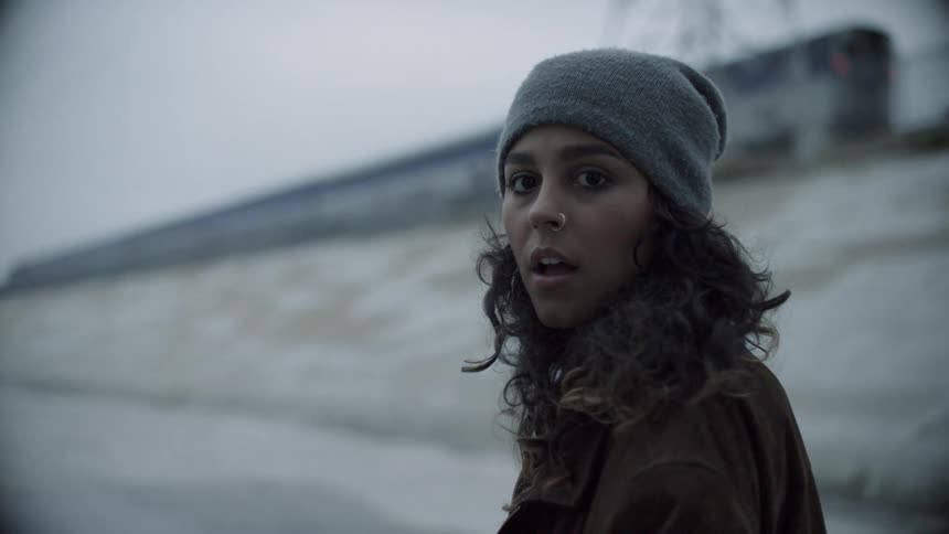 A woman stands beneath a moving train looking concerned and nervous