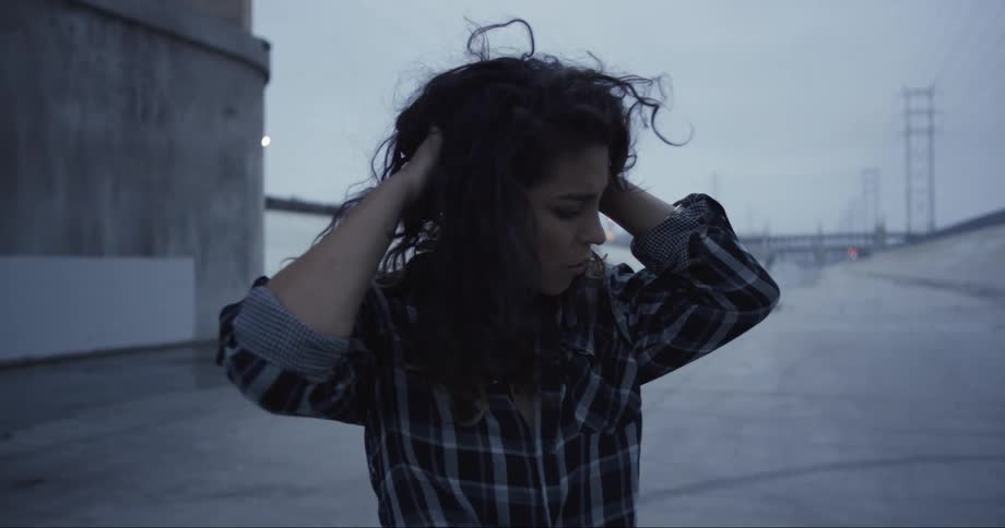 Woman standing under a bridge touches her hair