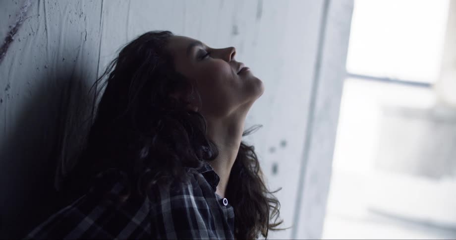 A woman leans against a wall and rolls her head around as she smiles