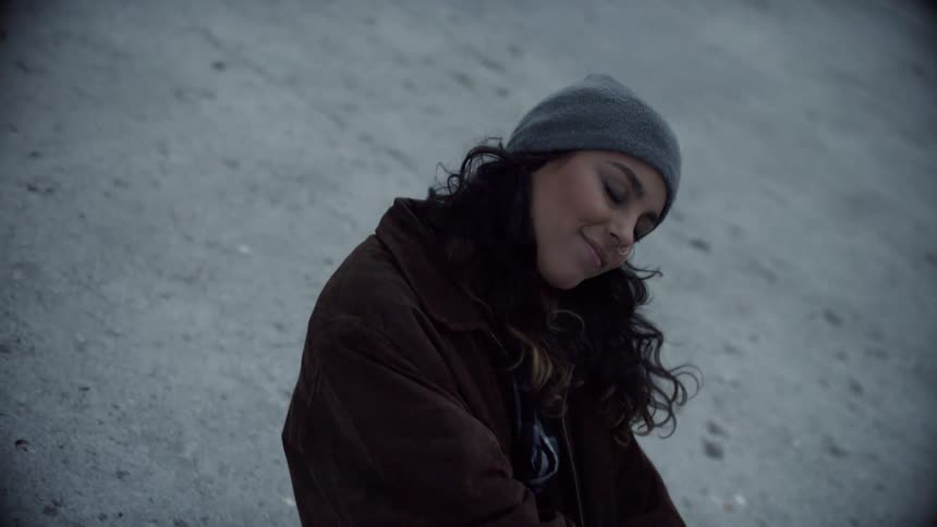 A teenager sits outside on the concrete and rolls her head around and smiles