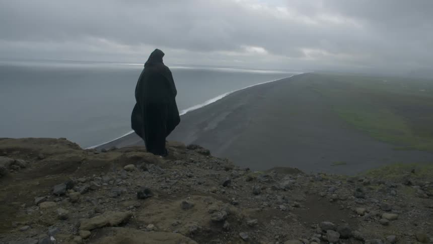 Black cloaked figure standing on a rocky edge of cliff