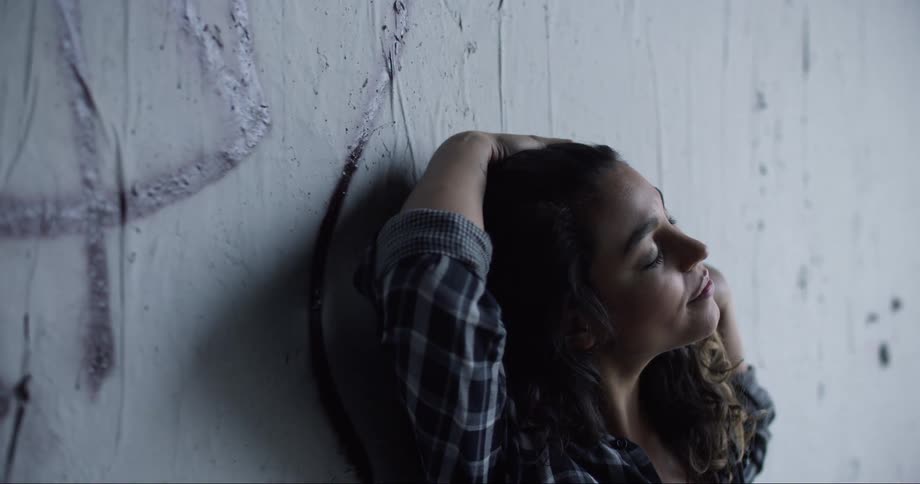 Brunette woman leaning her back against the wall caresses her hair