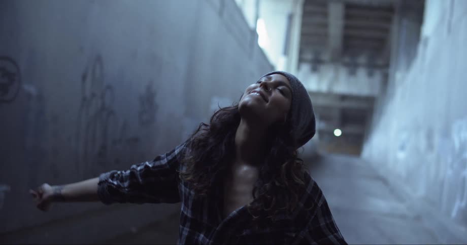 A woman dancing in a concrete corridor under a bridge