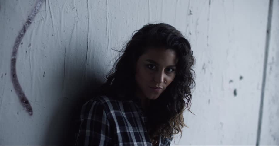 A woman leans against a wall and poses and looks at the camera in a sexy manner