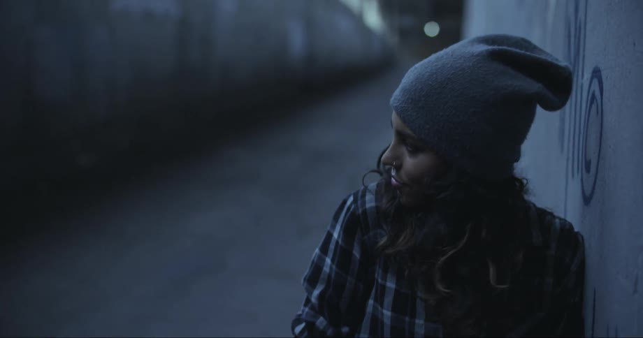 A young woman leans against a wall in a tunnel