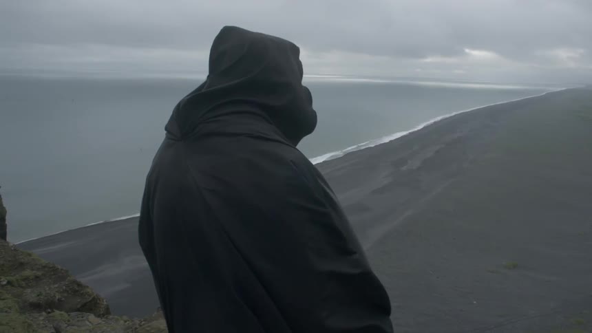 A person wearing a black robe is standing on the top of a mountain