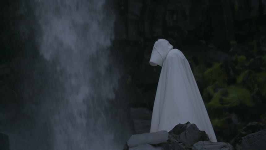 A person wearing white robes is standing near a waterfall
