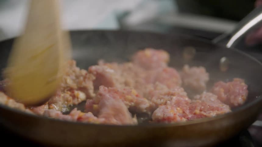 A person cooks meat in a pan