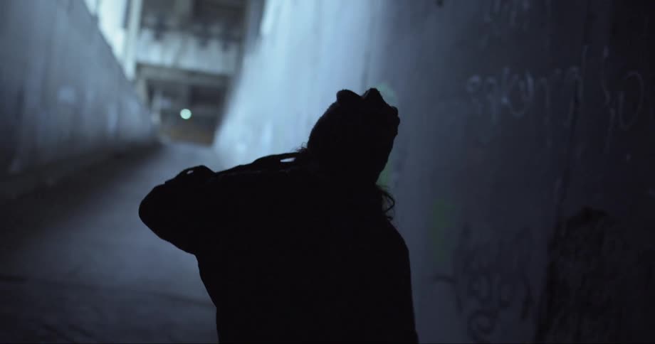 Woman cast into silhouette dances and walks along graffiti covered culvert