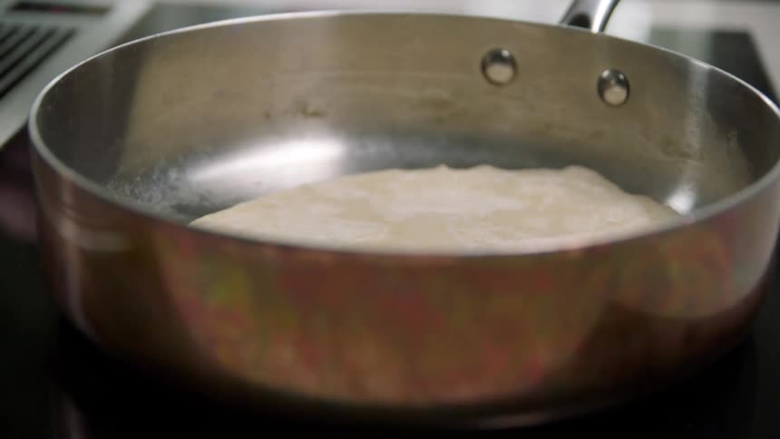 A person puts a flat bread on the pan