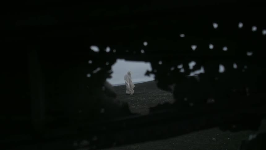 A cloaked figure walks alone outside