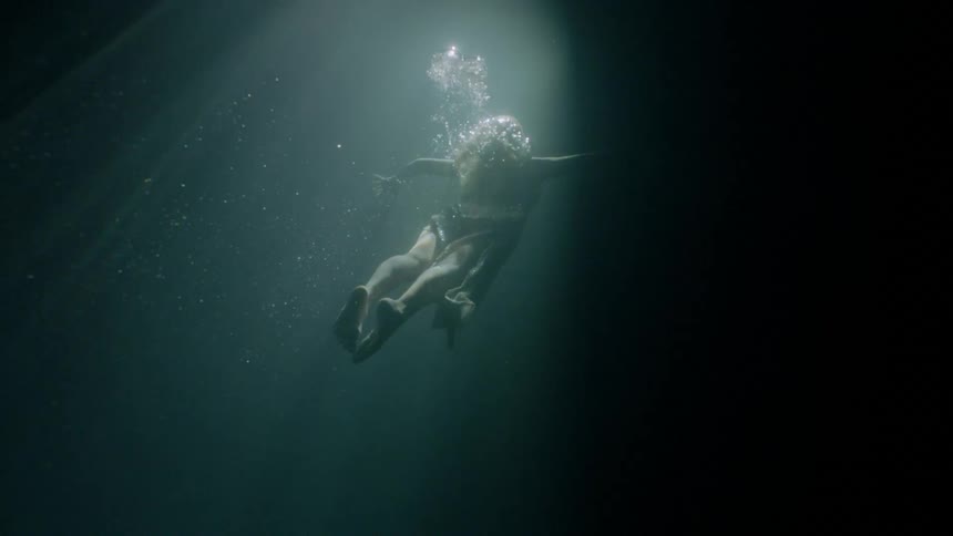 Woman wearing dress swims underwater towards the surface
