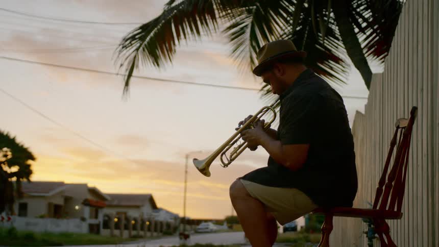 A man sits outside on a chair playing the trumpet