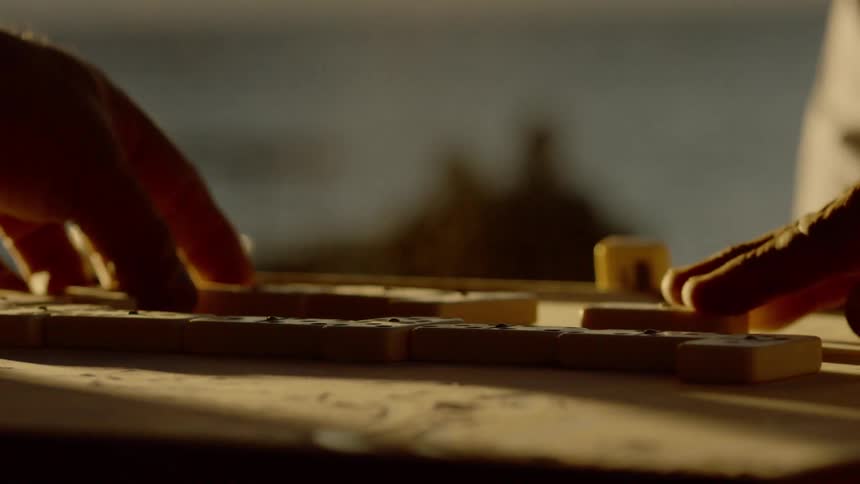Dust flies up from the table top when a man moves his domino tile and taps his fingers