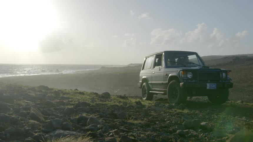 A person drives a vehicle across a field in front of the water
