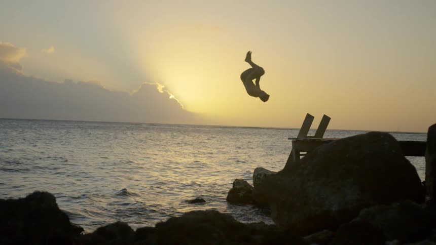 A man runs down a wooden dock and does a flip into the ocean at sunset