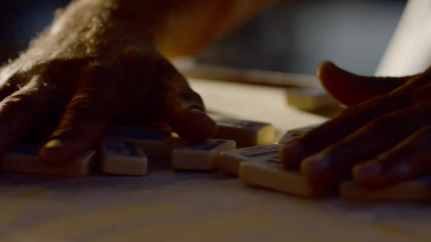 Person mixes dominoes tiles on dusty surface
