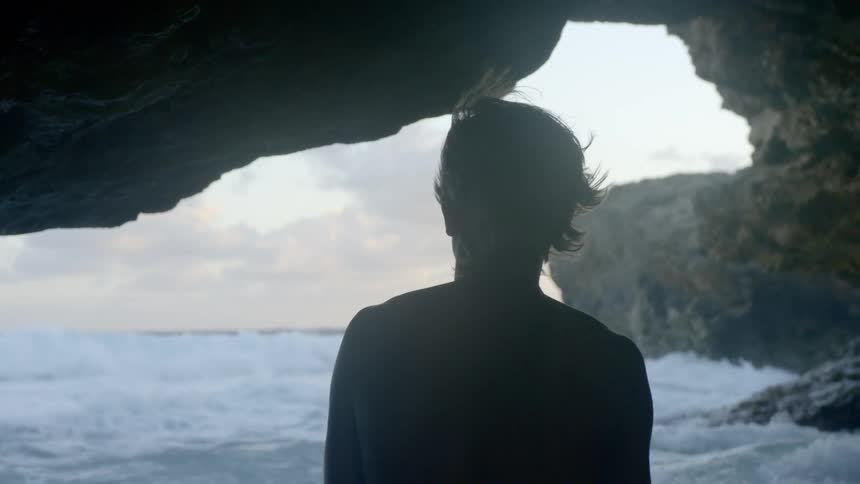 A man sits and looks out at the waves crashing in to the shore