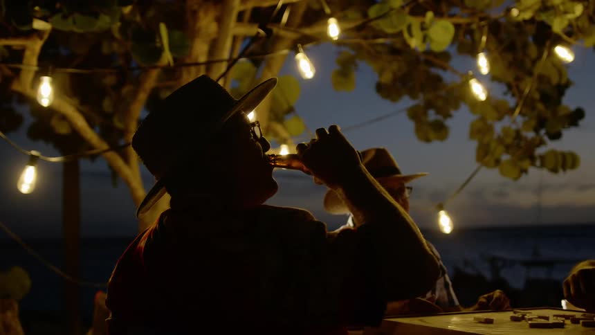 Three men sit at a table on the coast and drink beer and play dominoes