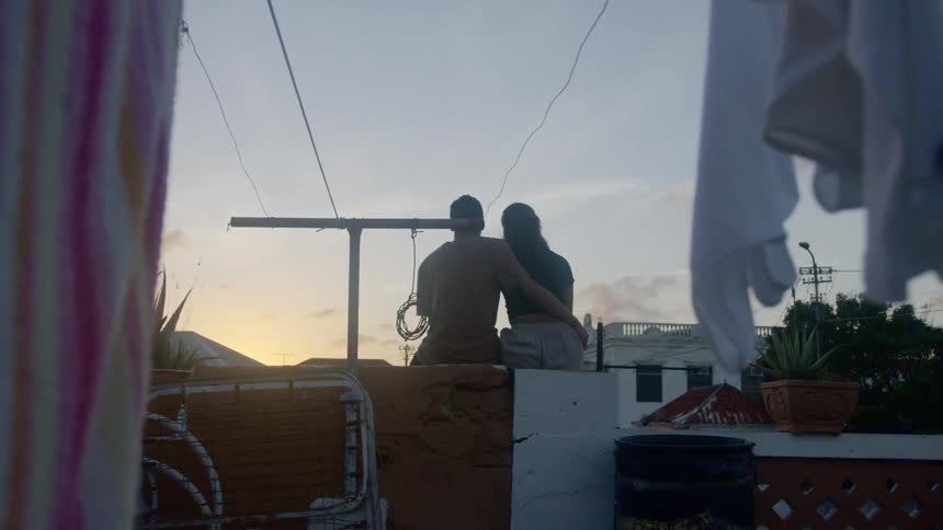 Couple sits on the rooftop of a house and watches the sunset