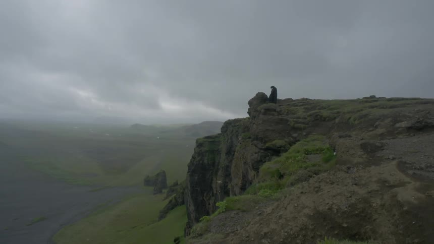 A lone person stands on a mountain cliff on a cloudy day
