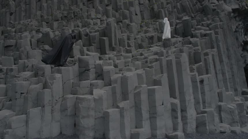 Two cloaked people standing on steep rock formations