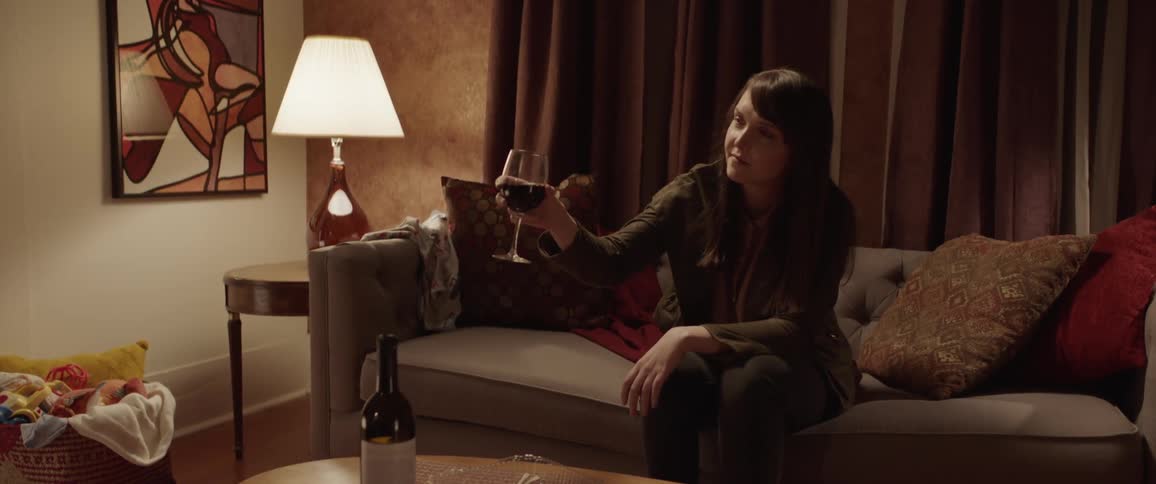 Woman sitting on couch in living room holding up wine glass