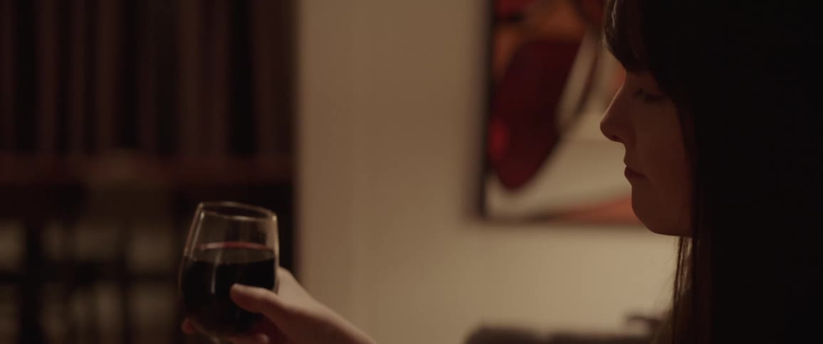 A woman sits at home and toasts someone with a glass of red wine