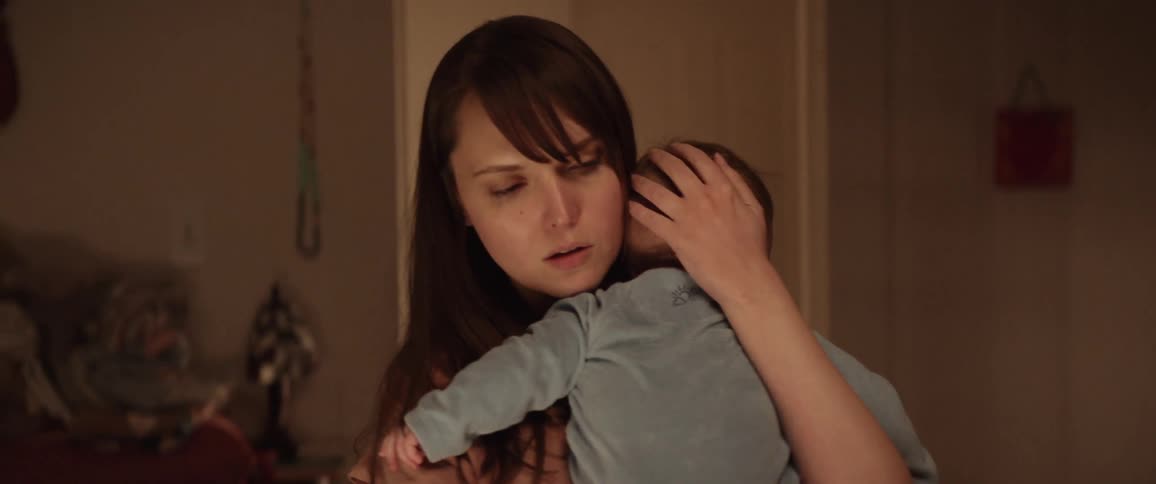 Mother with a concerned look on her face lovingly picks up her baby and puts his head up to her shoulder while gently stroking his head and rocking back and forth
