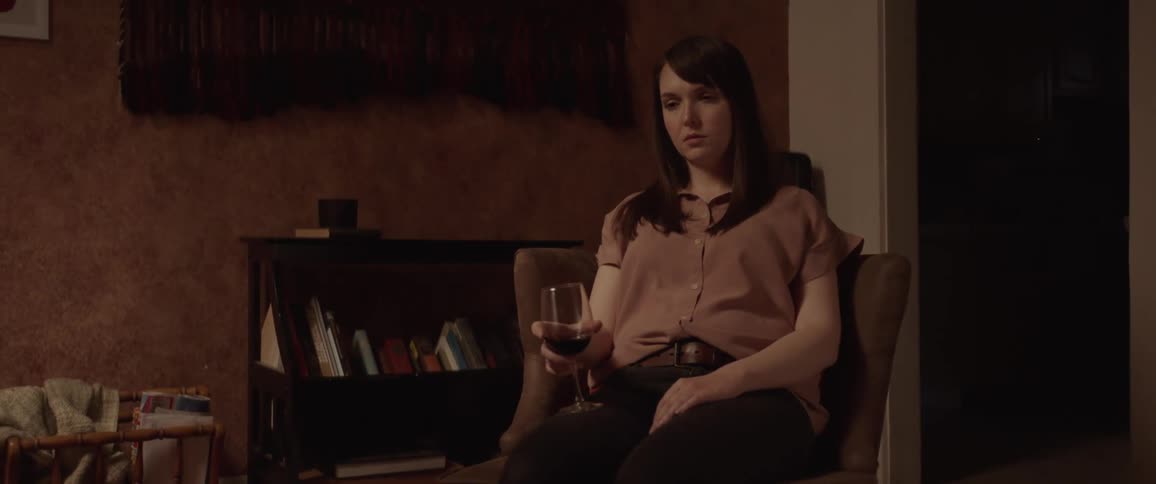 A very sad looking woman sits in a chair holding a glass of wine