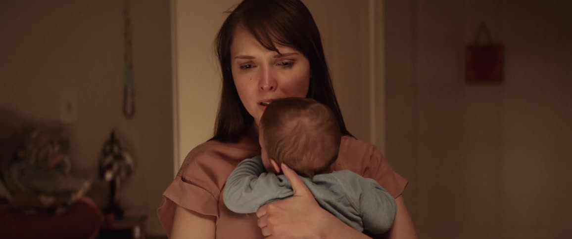 A woman is holding her baby indoors and looking sad