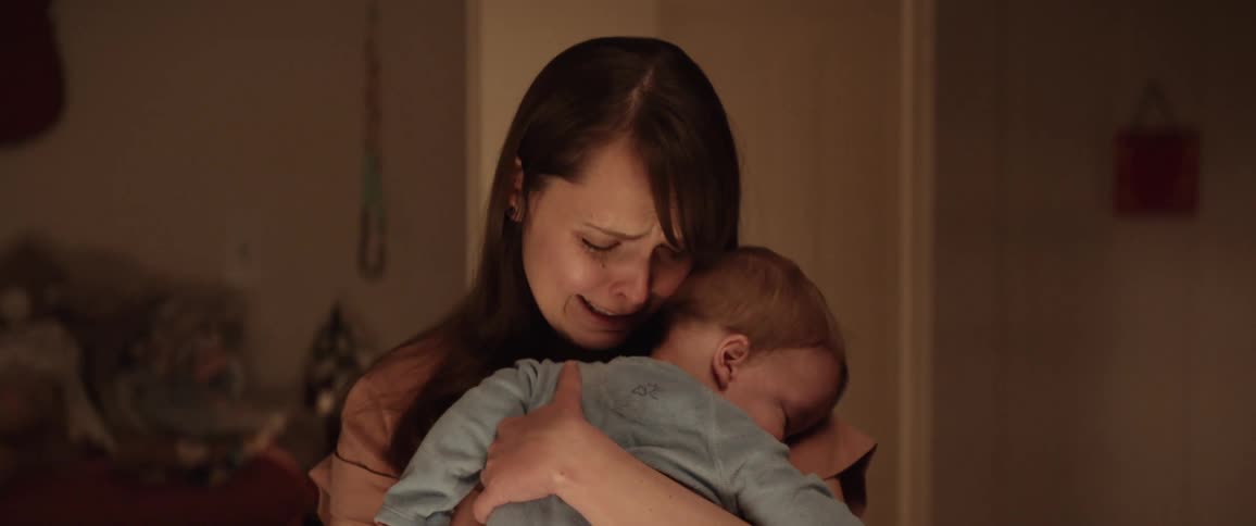 Distressed mother crying while holding sleeping baby at night