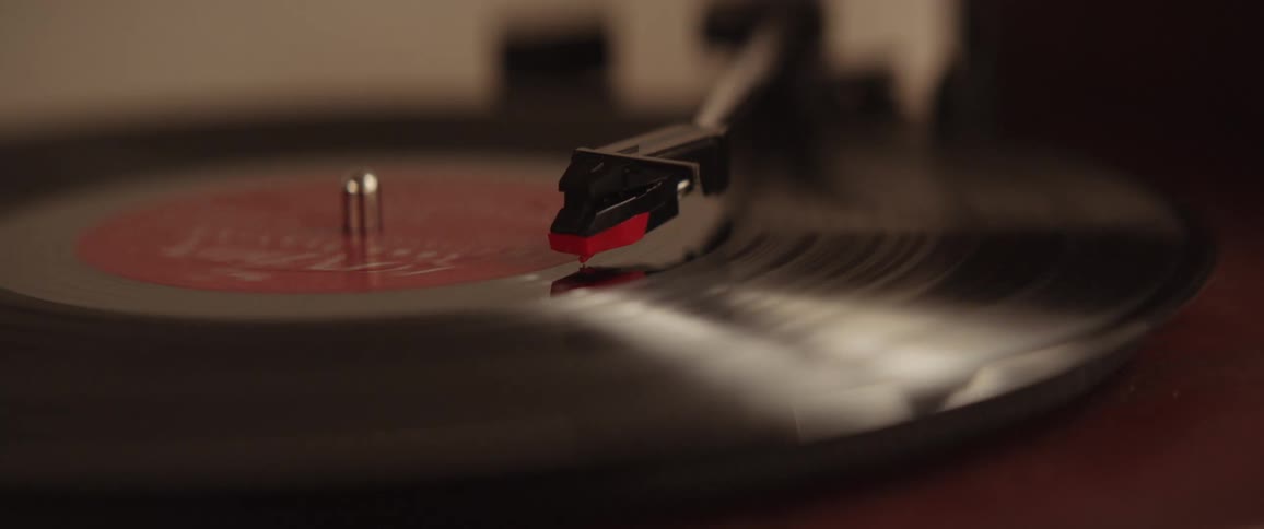 Arm of a record player sits on the record as the record spins