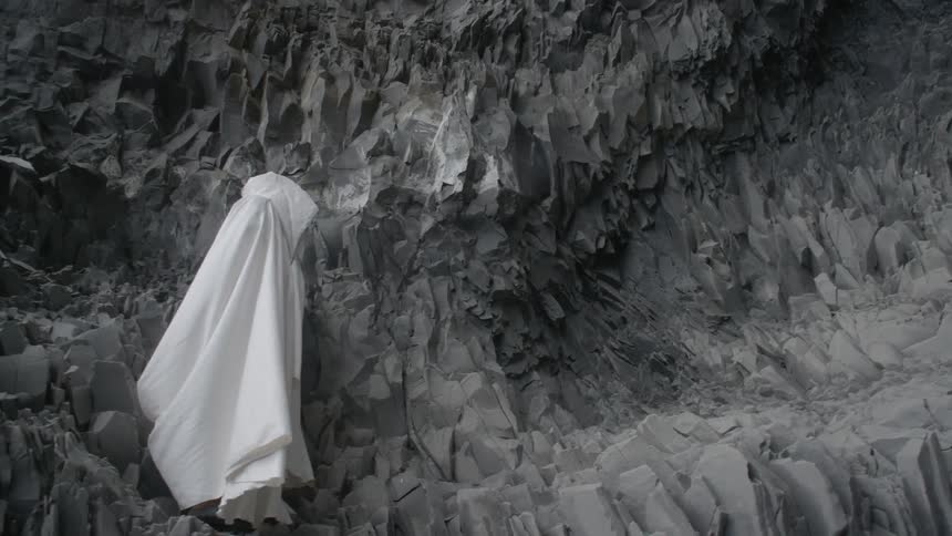A person wearing white robes is standing on the side of rock canyon