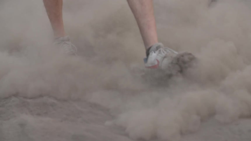 A person is walking in the dirt making clouds of dirt as he walks