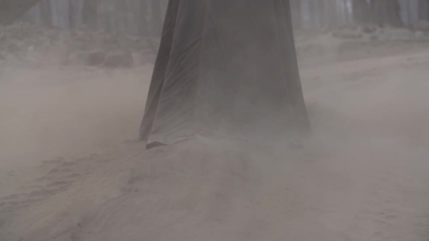 A person wearing black robes is walking over some sand