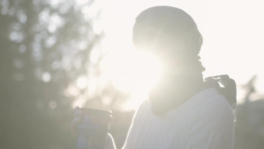 A woman holds a steaming mug outside on a chilly day
