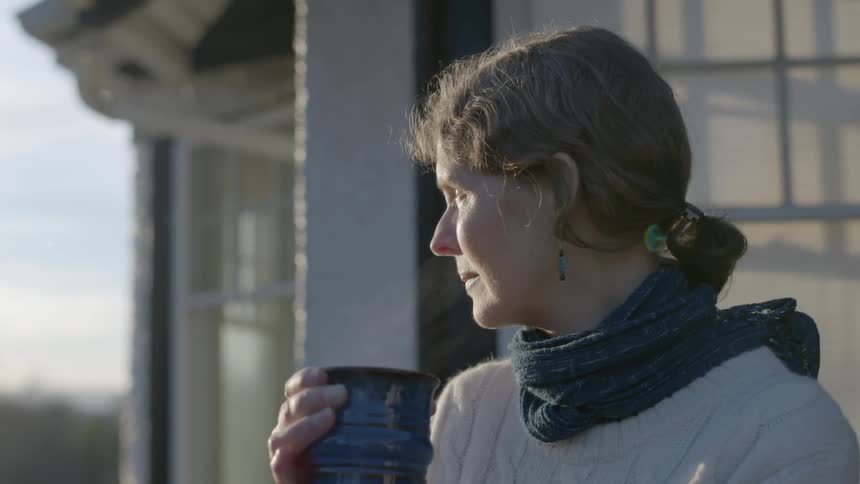 A woman holds a steaming mug outside her home on a chilly day