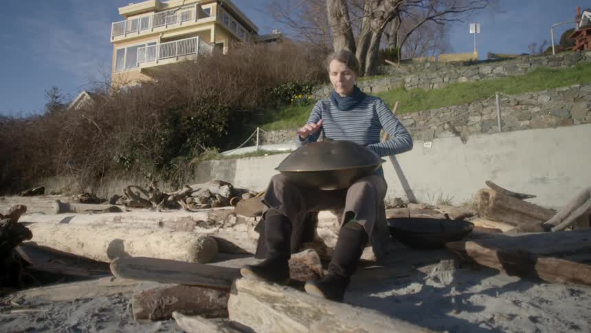 A woman is playing drums sitting on some rocks on a sunny day