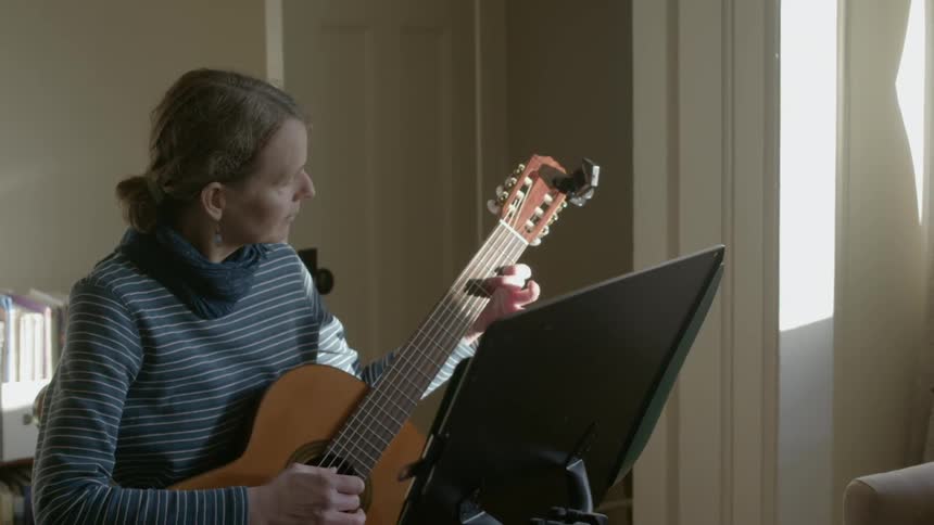 A woman is playing a guitar in front of sheet music